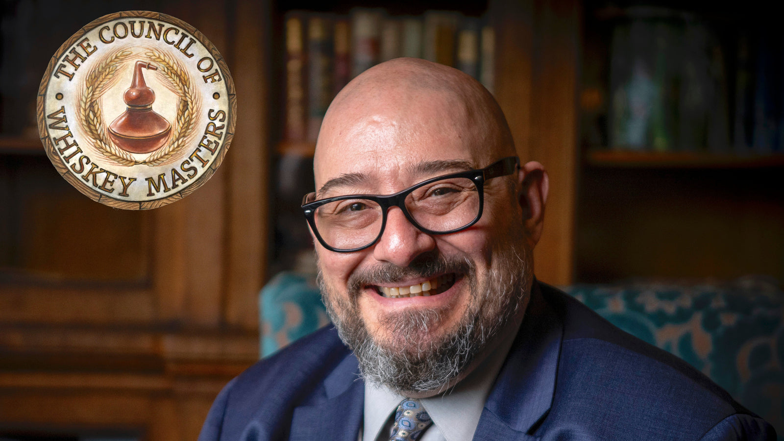 Man in a suit with a beard and glasses, smiling, in front of a bookshelf with 'The Council of Whiskey Masters' logo.