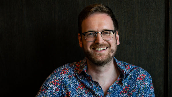 Man wearing glasses and a patterned shirt sitting at a table with a dark background
