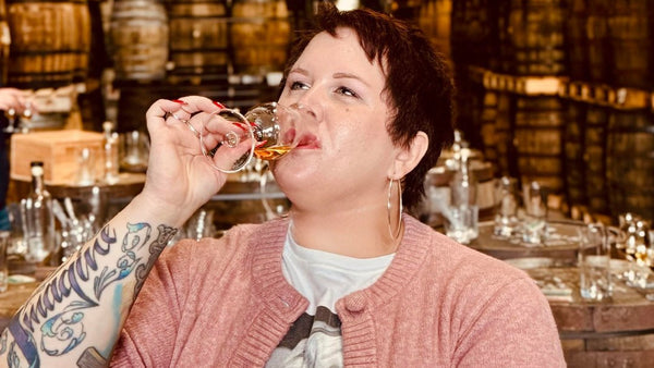 Person drinking from a glass in a bar with wooden barrels in the background