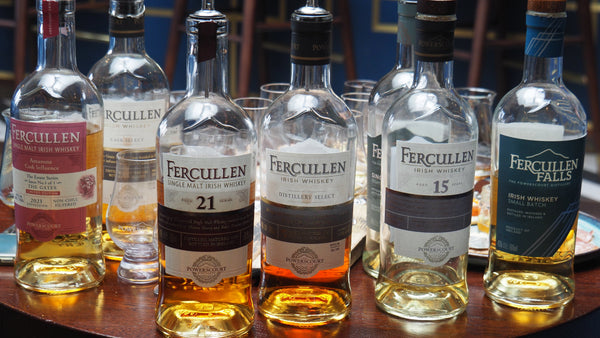 Collection of Fercullen whiskey bottles on a wooden table with glasses in the background.
