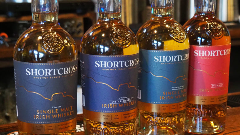 Four bottles of Shortcross whiskey on a bar counter with a blurred background