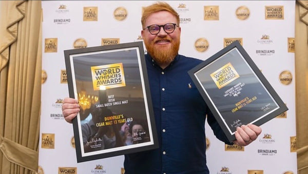 Man holding two framed awards against a branded backdrop