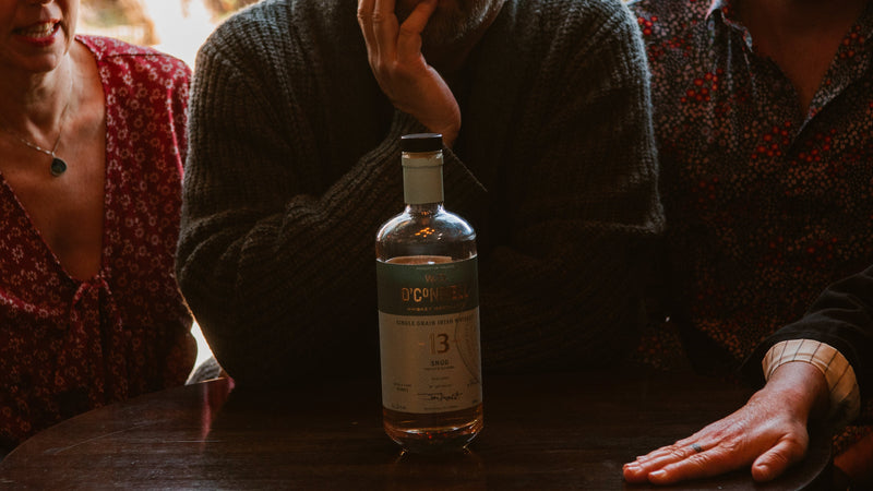 Three people sitting around a table with a bottle of whiskey in the center.